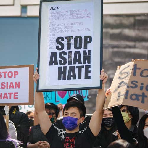 Person wearing a face mask while holding a "Stop Asian Hate" sign.