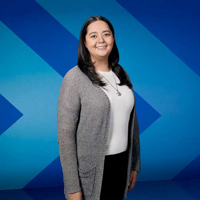 Dr. Johanna Sam, an assistant professor in UBC’s Faculty of Education and a citizen of the Tŝilhqot’in Nation, stands in front of a stylized chevron background.