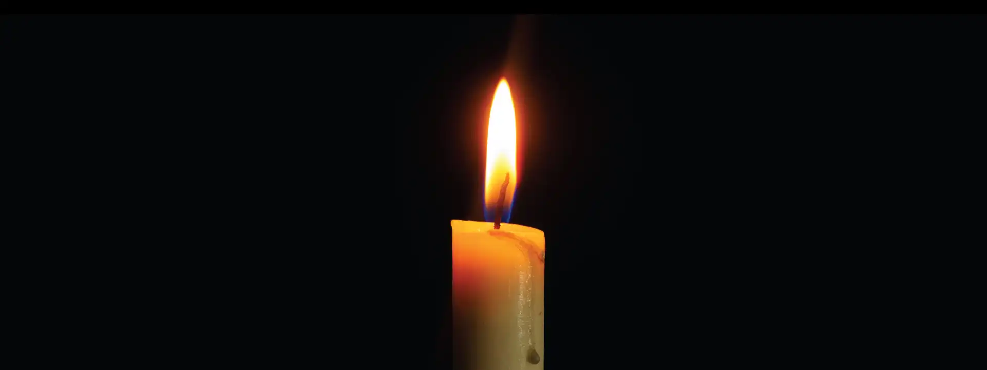 A lit wax candle on a black background