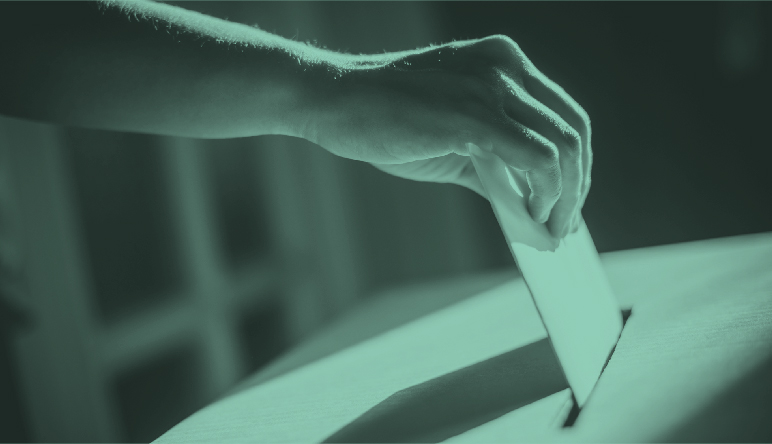 Hand placing an election ballot into a voting box.